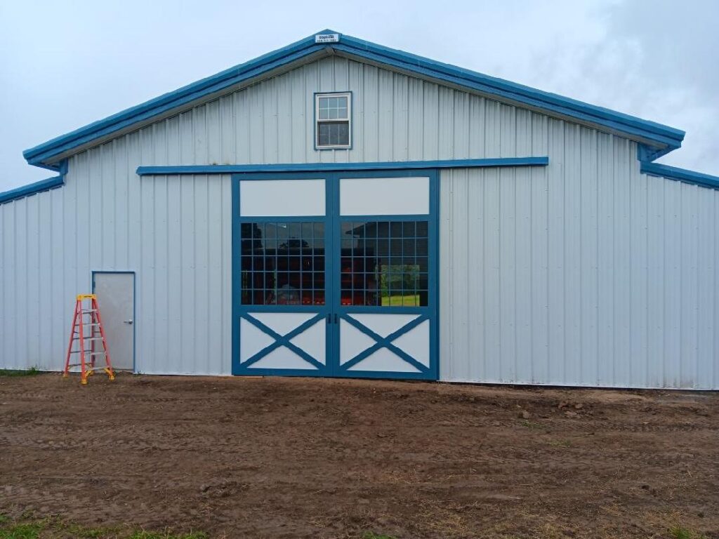 This 80'x80' steel building includes a wrapped 20' canopy porch on three sides. The main building has an 18" overhang and soffit on each side with gutters & downspouts. There is a 14'x14' slider door on the back side, 8'x8' opening on the other end, (6) 4x8 sidewall openings for individual horse stalls, a small window on each end and one 3070 walk door. The barn colors are Hawaiian Blue roof & trims with Polar White walls.