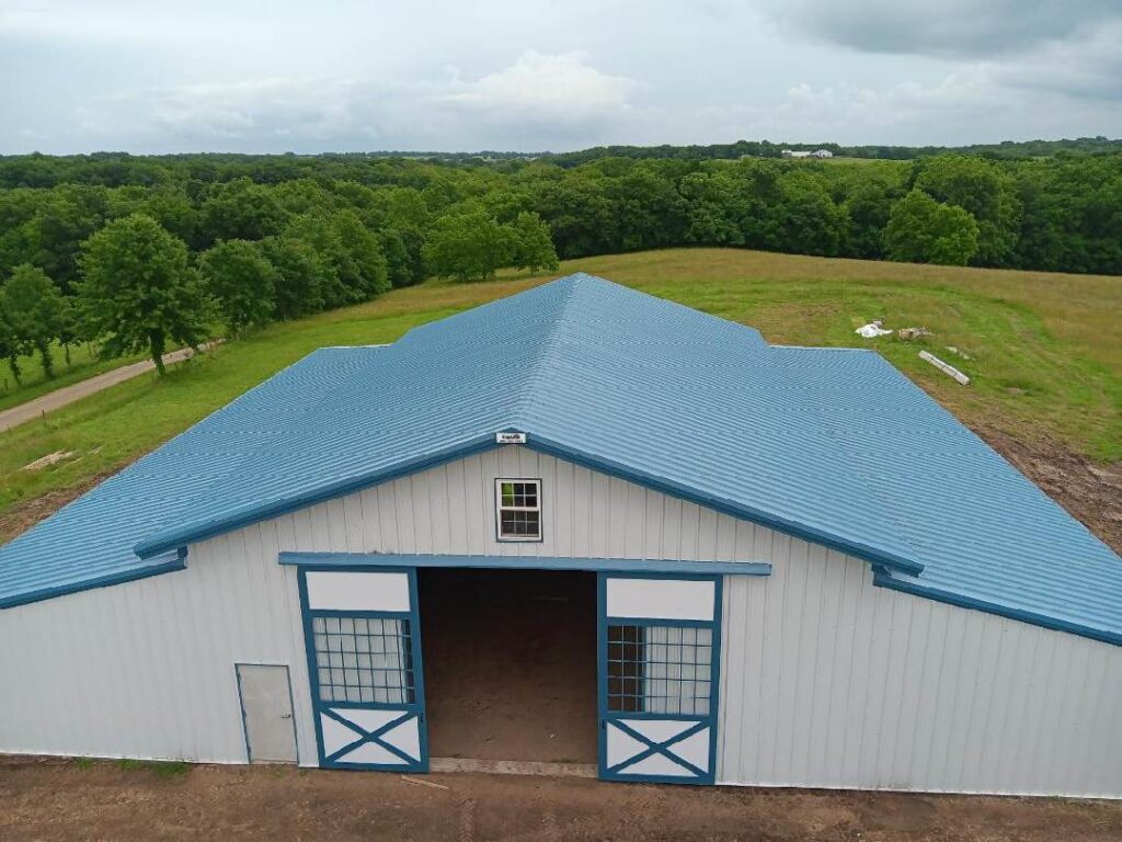This 80'x80' steel building includes a wrapped 20' canopy porch on three sides. The main building has an 18" overhang and soffit on each side with gutters & downspouts. There is a 14'x14' slider door on the back side, 8'x8' opening on the other end, (6) 4x8 sidewall openings for individual horse stalls, a small window on each end and one 3070 walk door. The barn colors are Hawaiian Blue roof & trims with Polar White walls.