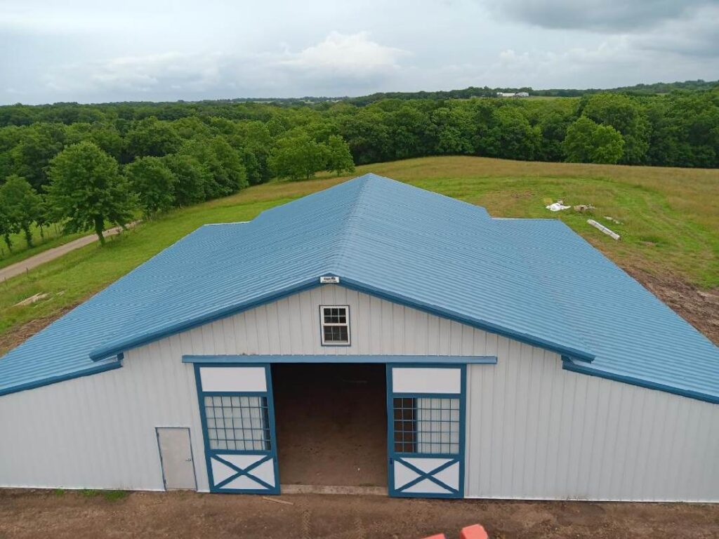 This 80'x80' steel building includes a wrapped 20' canopy porch on three sides. The main building has an 18" overhang and soffit on each side with gutters & downspouts. There is a 14'x14' slider door on the back side, 8'x8' opening on the other end, (6) 4x8 sidewall openings for individual horse stalls, a small window on each end and one 3070 walk door. The barn colors are Hawaiian Blue roof & trims with Polar White walls.
